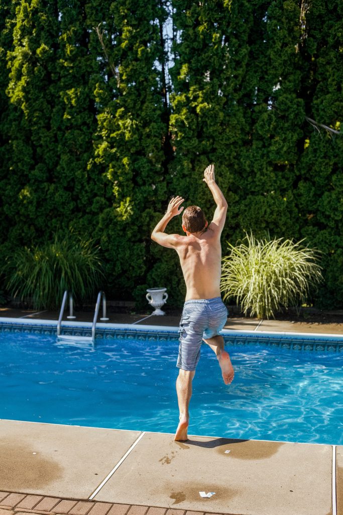 Boy jumping into pool surrounded by plants